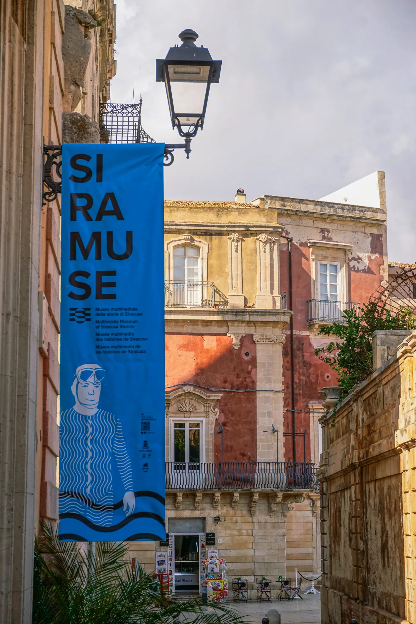 Blue Siramuse banner hanging from a baroque building in Ortigia